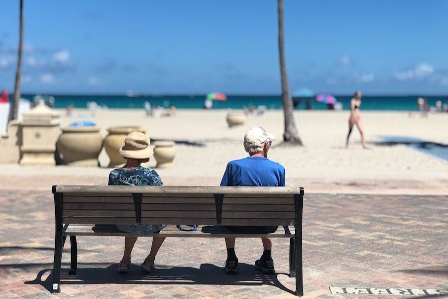 An older couple sat on a bench overlooking a sandy beach.