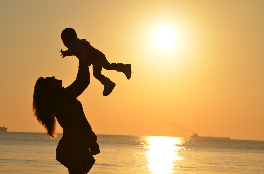 Mother throwing her child in the air in front of a sunset